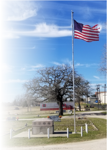 A Cemetery Monument next to Flag pole with a American Flag ontop.
